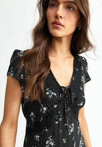 Vestito nero floreale con maniche a sbuffo corte, dettagli in pizzo sul collo e motivi di fiori blu su uno sfondo a pois.