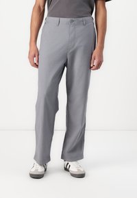 Gray, lightweight cotton trousers with a relaxed fit, featuring a button closure, and side pockets. Worn with white sneakers.