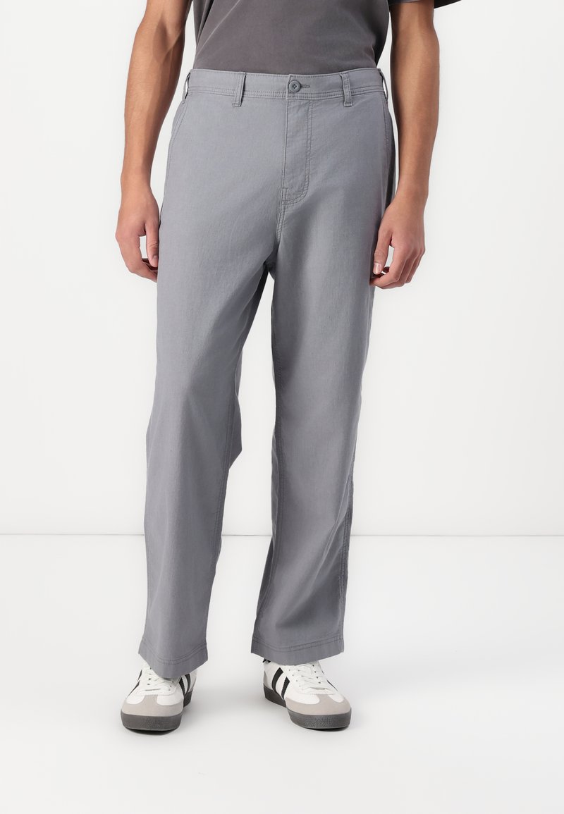 Gray, lightweight cotton trousers with a relaxed fit, featuring a button closure, and side pockets. Worn with white sneakers.