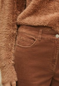 Pantalon en velours côtelé marron avec poches avant et un pull en laine marron texturé et duveteux. Le tissu semble doux et chaud avec une finition lisse.