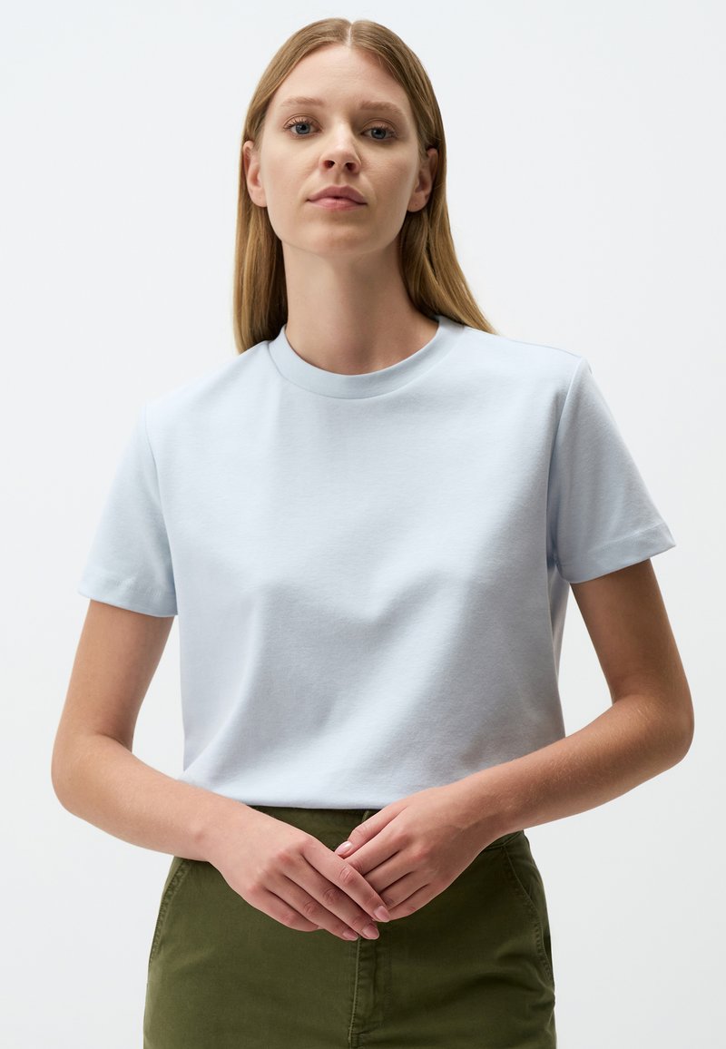 T-shirt in cotone azzurro chiaro con maniche corte, scollo rotondo e texture liscia, abbinato a una gonna verde. Design semplice e sobrio.