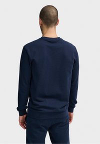 Granatowy sweatshirt z długimi rękawami, ściągaczami przy mankietach i u dołu, gładką fakturą i okrągłym dekoltem. Brak widocznych logo lub wzorów.