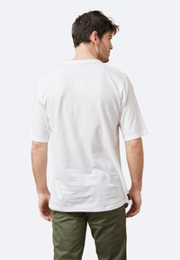 Camiseta blanca de algodón con mangas cortas, cuello redondo y un ajuste relajado, que se lleva sobre pantalones de color verde oliva. Sin patrones ni gráficos visibles.