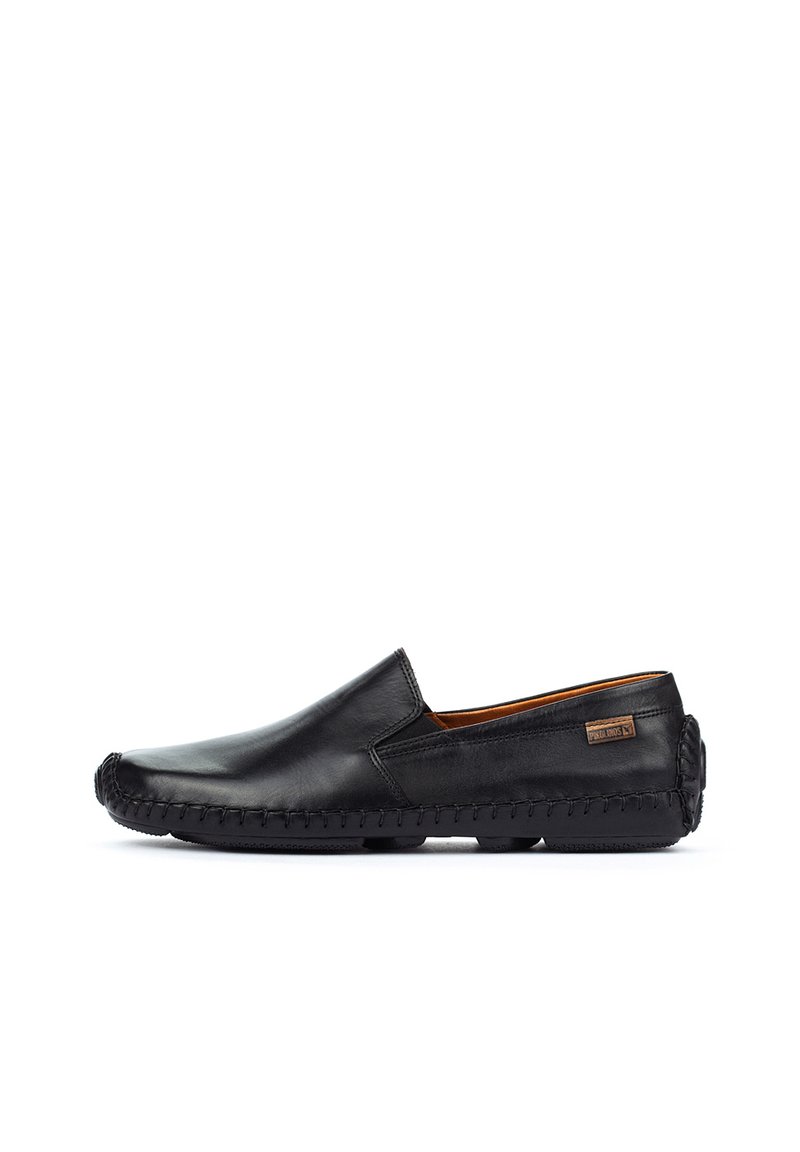 Zapatos negros de cuero tipo slip-on con un acabado suave, detalles de costura a lo largo de la suela y una etiqueta de marca marrón en el lateral.