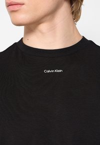 T-shirt noir en coton avec col rond et coupe ajustée, arborant un logo "Calvin Klein" blanc imprimé sur la poitrine.
