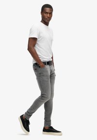 Vaqueros gris ajustados, camiseta blanca y zapatillas negras. Los vaqueros tienen un ligero desgaste y un diseño clásico de 5 bolsillos.