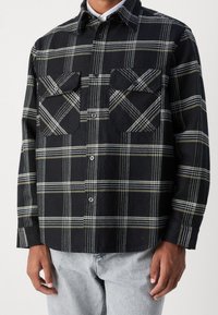 Schwarz-weiß kariertes Flanellhemd mit zwei Brusttaschen, Knopfverschluss, langen Ärmeln und abgerundetem Saum. Weicher, strukturierter Stoff.