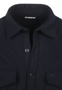 Donkerblauwe wollen overhemdjas met een puntige kraag, twee voorzakken en zwarte knopen. Heeft een label bij de nek. Zachte textuur.