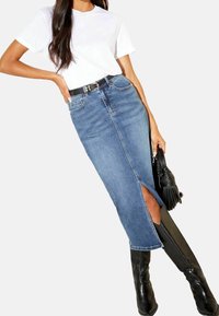 Jeanskjol med slits fram, i kombination med en kortärmad vit t-shirt och knähöga svarta stövlar. Inkluderar ett svart bälte och handväska.