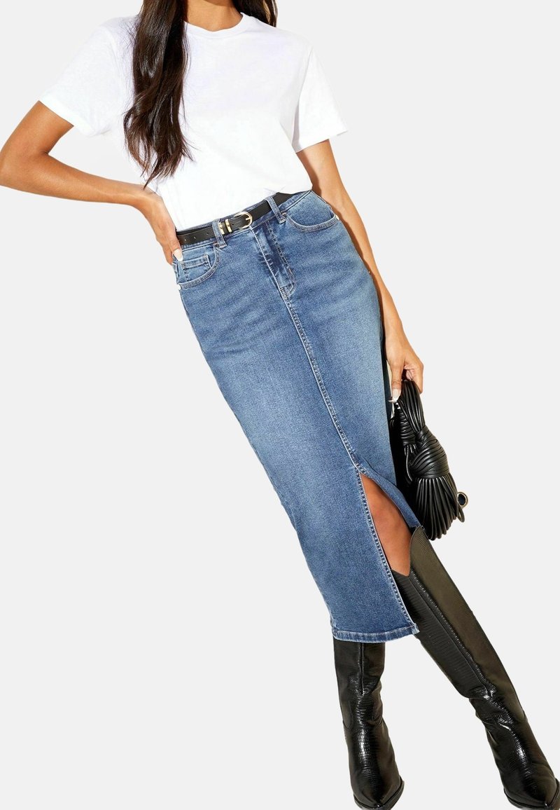 Jeanskjol med slits fram, i kombination med en kortärmad vit t-shirt och knähöga svarta stövlar. Inkluderar ett svart bälte och handväska.