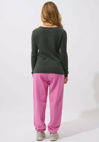 Maglione in maglia verde scuro con scollatura ampia abbinato a pantaloni della tuta rosa chiaro, dai tagli morbidi e dotati di polsini elastici.