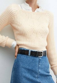 Pull en tricot pêche clair avec un motif floral, associé à une jupe en denim taille haute et une ceinture noire.