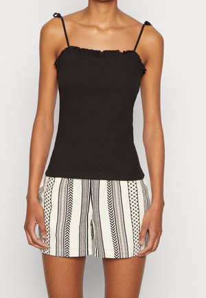 Top in cotone nero a coste con scollatura arricciata e spalline regolabili, abbinato a pantaloni corti bianchi con motivi geometrici e zigzag neri.