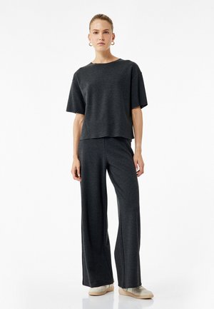 Top gris oscuro, de corte relajado y mangas cortas, combinado con pantalones de pierna ancha en tela a juego, que presentan una textura suave y un diseño minimalista.
