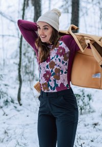 Květinový top s dlouhým rukávem v růžových a fialových odstínech, kombinovaný s tmavými kalhotami a světlým hnědým fleecovým bundou, na pozadí zasněženého lesa.