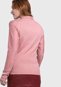 Hellrosa gerippter Langarmoberteil mit hohem Kragen und Daumenlöchern, mit einem eleganten Design und softem Material, kombiniert mit einem roten Rock.