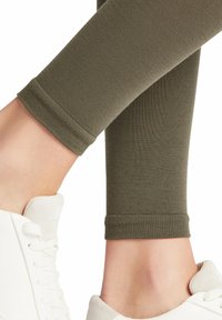 Olijfgroene leggings met een gladde textuur, voorzien van een getailleerd ontwerp en geribde boorden, gecombineerd met witte sneakers.