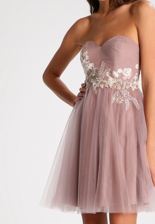 Robe mauve sans bretelles avec broderie florale autour de la taille et une jupe en tulle doux, portée par une personne debout avec la main sur la hanche.