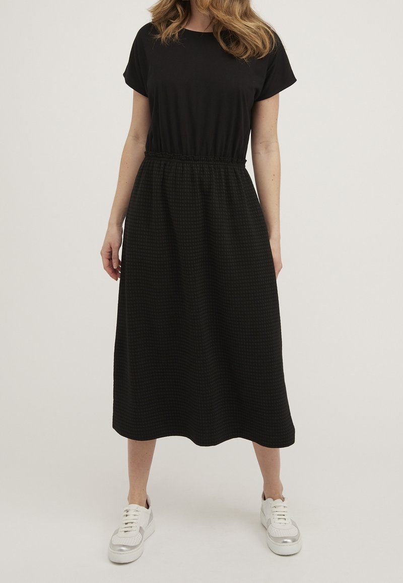 Vestido negro de manga corta con cinturilla elástica y falda texturizada con estampado, combinado con zapatillas blancas.