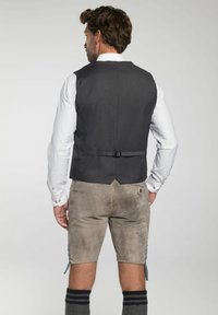 Grau strukturierte Weste mit verstellbarem Rückengurt, kombiniert mit hellbraunen Shorts. Weißes Hemd mit geknöpften Manschetten und knielangen grauen Socken.