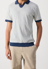 Pruhovaná polo košile v bílé a námořnické barvě, s výstřihem do V, krátkými rukávy s námořnickými manžetami a pevným námořnickým lemem. Textura z bavlněné tkaniny.