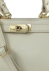 Lichtbeige handtas met een gestructureerde afwerking, gouden hardware en gedetailleerd stikwerk. De sluiting is een gouden rechthoekige gesp.