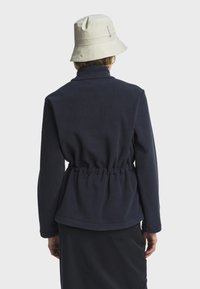 Chaqueta de forro polar navy con cintura ajustada, cuello alto y mangas largas. Lleva un sombrero tipo cubo beige. Tejido texturizado.