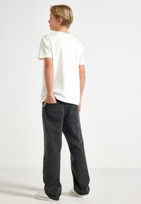 T-shirt bianco in cotone a maniche corte abbinato a jeans in denim neri; i jeans presentano tasche posteriori e una vestibilità comoda, completati da sneakers bianche.