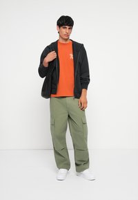 Sort zip-up hoodie over en orange t-shirt. Oliven grønne cargo bukser med sidelommer og hvide sneakers. Minimalistisk design og afslappet pasform.