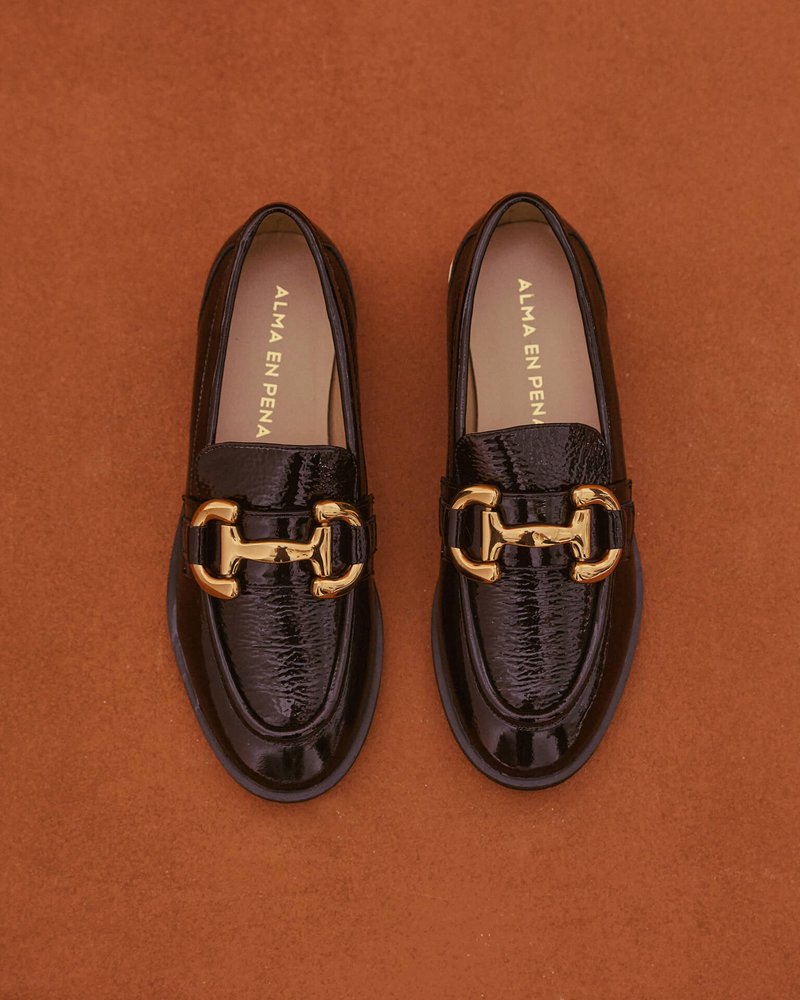 Mocassini in vernice nera con dettaglio in catena dorata, texture liscia, punta arrotondata e design classico senza lacci.