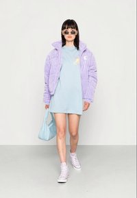 Casaco acolchoado lavanda com riscas verticais, t-shirt azul clara com gráfico, vestido curto, mala azul clara e sapatilhas cor-de-rosa.