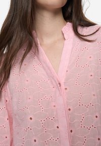 Roze geborduurde top met bloemvormige uitsparingen, met een halfdoorzichtige textuur, een opstaande kraag en een knoopsluiting aan de voorkant. Zachte, lichtgewicht stof.