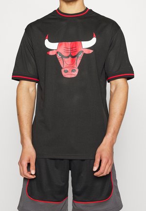 Osoba ubrana w czarną sportową siateczkową odzież z czerwono-białym logo Chicago Bulls na koszulce oraz pasujące czarno-szare spodenki z czerwonym wykończeniem.