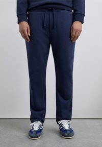 Pantalones deportivos azul marino con cintura ajustable con cordón, que presentan una textura suave y un ajuste entallado. Zapatillas deportivas blancas y azules con cordones.