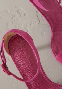 Fuksia vaaleanpunaiset korkokengät, joissa on sileät ja teksturoidut pinnat, nilkkapantoja ja prässätty logo sisäpohjassa.