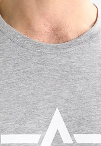 Gray crewneck T-shirt with a smooth texture, featuring a white graphic design at the chest. Neckline is ribbed for added durability.