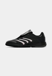 Scarpa sportiva nera con design elegante, tomaia in materiale sintetico, accenti a strisce bianche, modello basso e una fascia in velcro sulla parte superiore del piede per una vestibilità sicura.