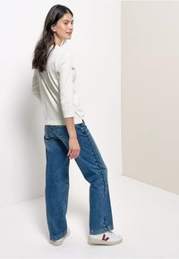 Light gray long-sleeve top with a round neckline paired with blue wide-leg jeans, completed with white sneakers featuring maroon accents.