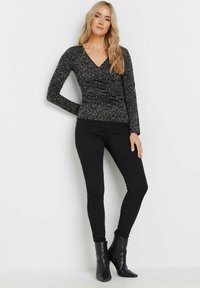 Maglietta nera a maniche lunghe con scollatura a V, caratterizzata da un tessuto testurizzato e a fantasia. Indossata con jeans skinny neri e stivaletti.