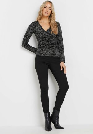 Zwarte longsleeve top met V-hals, vervaardigd uit een textuur met een patroon. G gedragen met zwarte skinny jeans en enkellaarzen.