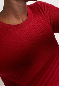 Red ribbed knit sweater featuring a round neckline and long sleeves, showcasing a textured fabric with vertical stripes.