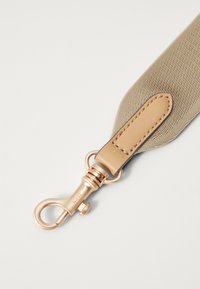 Cinghia in tessuto beige con superficie testurizzata, caratterizzata da un accento in pelle color tabacco e una clip e hardware in metallo dorato all'estremità.