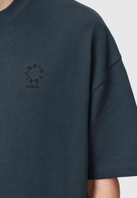 Ciemnoniebieski, oversize'owy t-shirt wykonany z bawełny, z prążkowanym dekoltem. Posiada haftowane logo po lewej stronie klatki piersiowej.