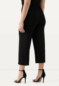 Černé culottes s elastickým pasem a zúženými nohavicemi, doplněné černými sandály na vysokém podpatku. Hladká tkanina s jemným leskem.