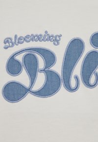 Biely textil s modrou výšivkou nesúcou nápis „Blooming Bl“ v dekoratívnom, zakrivenom písme. Dizajn má textúrovaný, prešívaný vzhľad.