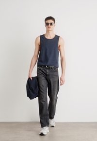 Mørkeblå ermeløs topp, mørke jeans, og lyse joggesko. Modellen bærer en mørkeblå hettegenser. Tilbehør inkluderer solbriller. Enkel, uformell stil.