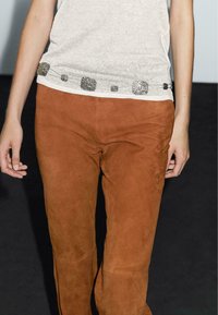 Beige topp med svart texturerad design längs fållen; kombinerad med figurnära bruna mockabyxor. Enkel, avslappnad outfit.