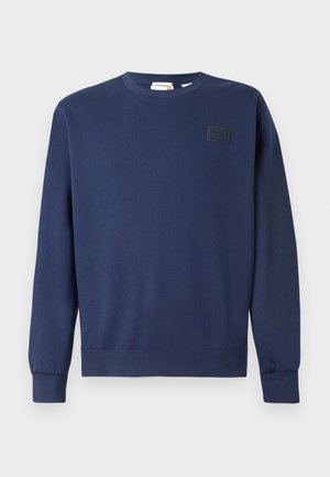 Námořnická modrá mikina vyrobená z měkké směsi bavlny, má kulatý výstřih, žebrované manžety a texturovanou nášivku loga na hrudi.