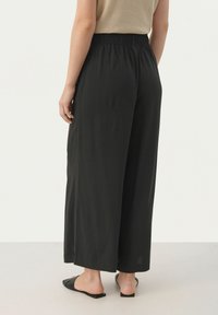 Pantalons larges noirs en tissu léger avec une taille élastique. Texture lisse avec une coupe décontractée, arrivant au milieu du mollet. Design minimaliste.