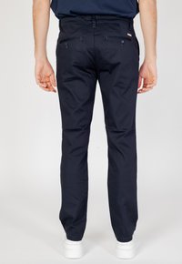 Pantaloni blu navy a taglio slim, realizzati in un morbido tessuto misto cotone. Presentano due tasche posteriori e passanti per cintura, abbinati a sneaker bianche.